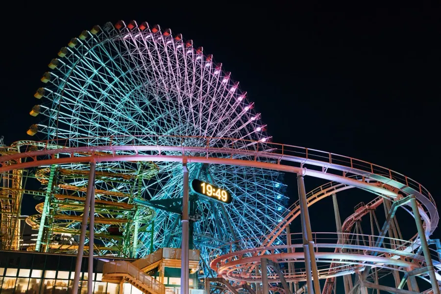 Grande roue colorée et montagnes russes illuminées dans un parc d'attractions la nuit