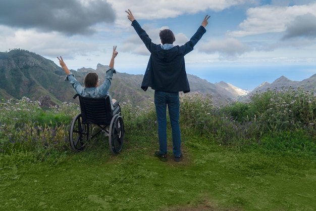 Vue de dos d'un couple, femme en fauteuil roulant, admirant un paysage de montagne ensemble